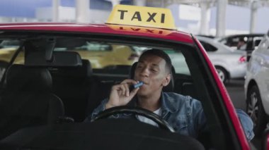 Gülümseyen Afrikalı Amerikalı taksi şoförü e-sigara içiyor. Servis arabası, sağlık hizmeti konsepti. Yavaş çekim