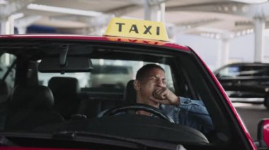 Yorgun erkek taksi şoförü arabada kahve içerken esniyor. Sarı taksi arabası tabelası. İnsanlar, iş, hizmet kavramı. Yavaş çekim