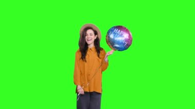 Gülümseyen stil sahibi bir kadın elinde renkli bir balonla, kutlama yapıyor ve yeşil izole bir arka plana öpücük yolluyor. Tatil, parti doğum günü konsepti