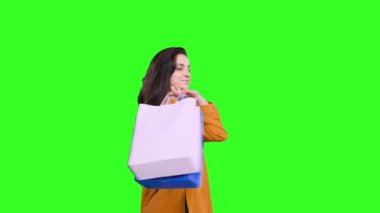 Sırıtan genç bir kadın çantaları omuzunda tutuyor, yeşil izole arkaplandaki kameraya bakıyor. Kara Cuma, satış konsepti