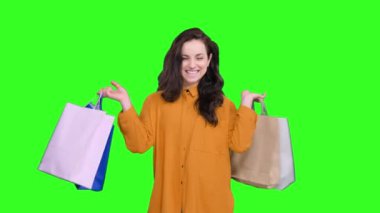 Renkli alışveriş torbaları taşıyan gülümseyen güzel kadın yeşil izole arka planda alışverişin tadını çıkarıyor. Kara Cuma, satış konsepti