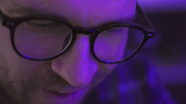 Dijital cihazını kullanıp gülümserken siyah gözlük takan yakışıklı bir genç. Gözlüklere yansıyan ekran. Yavaş çekim