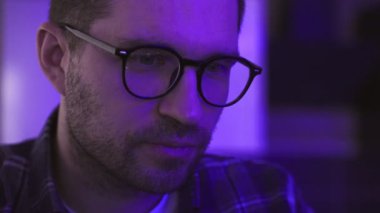 Kafkasyalı bir adam cihaz ekranına bakıyor, DJ parti programını izliyor, gözlükteki yansımasını görüyor. Performans, müzisyen, dans konsepti. Yavaş çekim