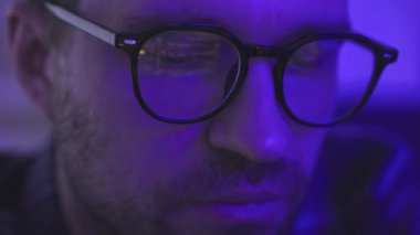 Çalışırken gözlük takan genç bir işadamı yatırım fonlarını analiz ediyor. Dijital, ticaret, yatırım, teknoloji konsepti. Yavaş çekim
