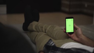 Kanepede dinlenen ve krom anahtar yeşil ekranlı cep telefonu kullanan bir adam. İnternet, iletişim konsepti, kapatın. Yavaş çekim