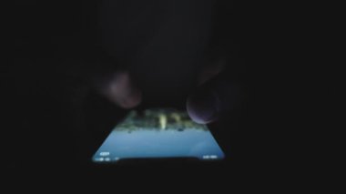 Karanlıkta parmaklarıyla ekranı silerken akıllı telefon kullanan bir erkek. Teknoloji, internet, online, mobil uygulama kavramı. Yavaş çekim