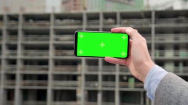 Erkek eli, yeşil ekranlı akıllı telefonu hareket ettiriyor ve bitmemiş çok katlı ev boyunca işaretleri takip ediyor. Yavaş çekim