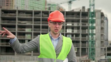 Çok katlı bir evin yanında dururken planlı bir inşaat müfettişi biriyle konuşuyor. Yavaş çekim