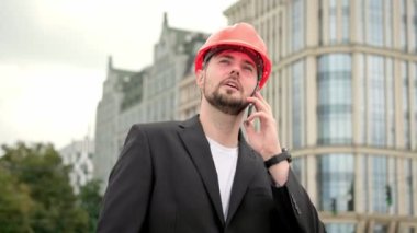 Ofis elbisesi ve koruyucu turuncu kasklı akıllı telefon, arıyor ve konuşuyor. Yavaş çekim videosu