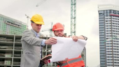 İki müteahhit büyük bir plan açar, siteye bakar ve tartışırlar. Yavaş çekim videosu
