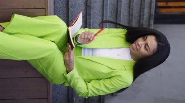 Amerikalı kadın dışarıda oturuyor, elinde defter, okuyor ve notlar alıyor. Yavaş çekim videosu. Öğrenim kavramı