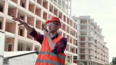 İnşaat işçisi, bitmemiş çok katlı binaların arasında dikilirken telsizle iletişim kuruyor. Yavaş çekim
