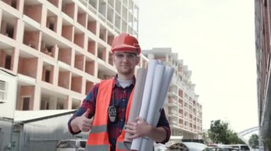 Bitmemiş binalar arasında duran ve kamera önünde baş parmak işareti veren gülümseyen inşaat müfettişinin belden yukarı portresi. Yavaş çekim