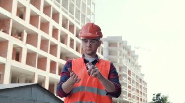 Tamamlanmamış yeni binaların arasında dikilirken avuç içine dezenfektan sıkan odaklı inşaatçının belden yukarı portresi. Yavaş çekim
