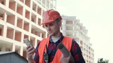 Ustabaşının portresi telsiz ve planlarla akıllı telefon ekranında bir şeyler okurken yarım kalmış çok katlı evlerin arasında duruyor. Yavaş çekim