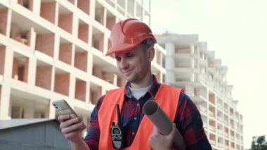 Çizimleriyle gülümseyen inşaat müfettişinin portresi ve bitmemiş çok katlı binanın yanındaki cep telefonundan haber okuyan telsiz telsizi. Yavaş çekim