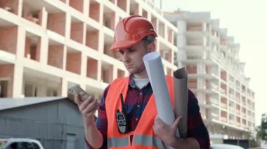 Planları ve telsizi olan bir ustabaşı, yarım kalmış çok katlı binanın önünden geçerken akıllı telefondan arıyor. Yavaş çekim