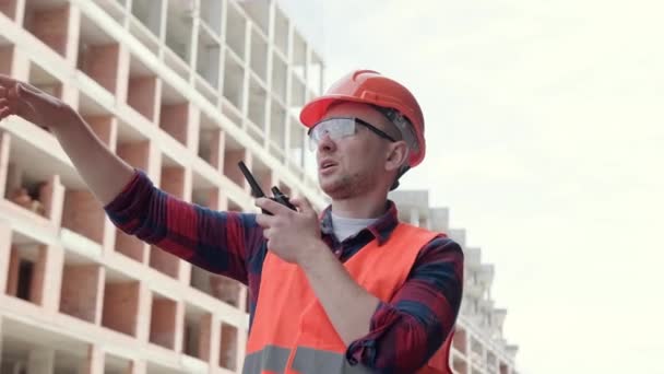 Foreman Stojí Mezi Nedokončenými Vícepodlažními Budovami Gestikuluje Mluví Vysílačkou Zpomalený — Stock video