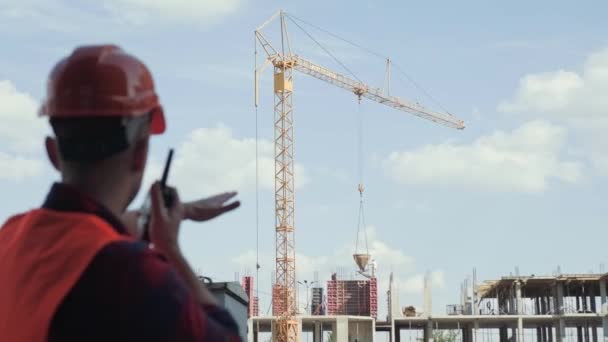 Építésvezető Kétirányú Rádión Beszél Miközben Daru Leeresztő Anyagokat Néz Befejezetlen — Stock videók