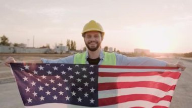 Foreman koruyucu miğfer ve yelek giymiş, elinde ABD bayrağı ve gülümsüyor. Yavaş çekim videosu