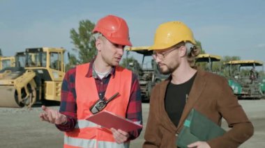 Profesyonel bir adam ustabaşıyla arabaların yanında yürüyüp, çalışma sürecini tartışır. Yavaş çekim videosu