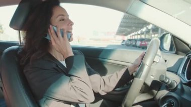 Akıllı telefon tutan bir kadın, park yerinde araba süren ve internetten arayan bir kadın. Yavaş çekim videosu