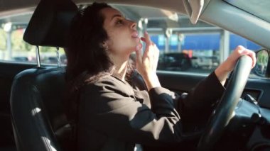 Park yerinde araba süren bir kadın, aynaya bakıyor ve parmaklarıyla ruj sürüyor. Yavaş çekim videosu