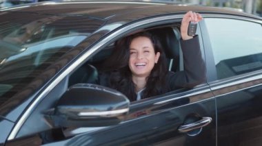 Gülümseyen iş kadını arabada oturuyor, elinde anahtarlar, kameraya gösteriyor ve gülümsüyor. Yavaş çekim