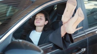 Topuklu ayakkabılı genç bayan arabanın camını açtı, arabada oturuyor ve dinleniyor. Gözlüklerini çıkar. Yavaş çekim videosu