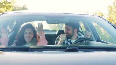 Olumlu genç çift araba sürerken, müzik dinlerken ve dans ederken eğleniyor. Ulaşım, seyahat, ilişki, insan konsepti. Yavaş çekim