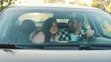 Romantik genç bir çift, arabada otururken birbirlerine sarılıyorlar. Ulaşım, seyahat, ilişki, insan konsepti, ağır çekim