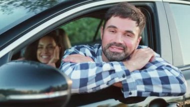Mutlu bir adam kız arkadaşıyla birlikte açık pencereden dışarı bakarken arabayla seyahat ediyor. Ulaşım, seyahat, ilişki, insan konsepti. Yavaş çekim