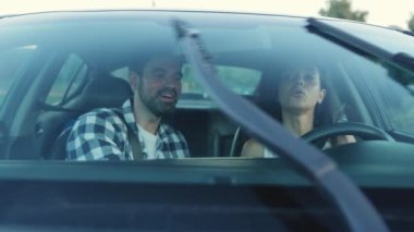 Gülümseyen genç adam direksiyon başında araba kullanmayı öğretiyor. Silecekler hareket ediyor. Ulaşım, seyahat, ilişki, insan konsepti. Yavaş çekim