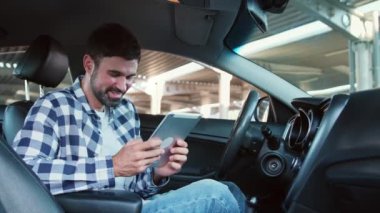 Arabada tablet ekrana bakarken gülen genç adam. Ulaşım, teknoloji, yaşam tarzı konsepti. Yavaş çekim