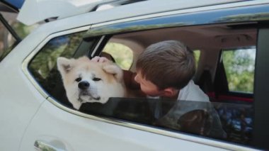Gülümseyen küçük çocuk, yolculuk sırasında köpeğiyle birlikte arka koltukta oturuyor, arabadan dışarı bakıyor. Seyahat, hayvan bakımı konsepti. Yavaş çekim