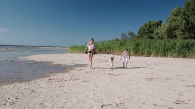 Gülümseyen kadın ve küçük çocuk deniz kıyısında köpekleriyle koşuyorlar. Aile, yaz tatili konsepti. Yavaş çekim