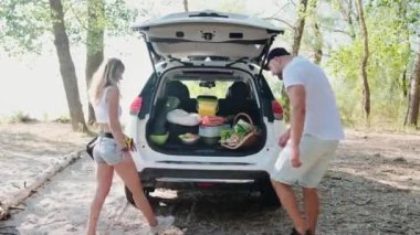 Gülümseyen adam ve kadın ormanda piknik yapmak için açık bagajdan yiyecek çıkarıyorlar. Hafta sonu, seyahat, aktif tatil konsepti. Yavaş çekim