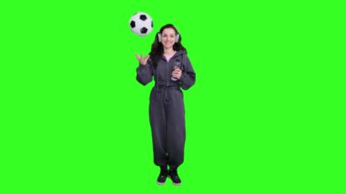 Futbol topuyla oynarken kulaklık takan ve yeşil alanda su tutan mutlu genç bir kadın. Tam uzunluk
