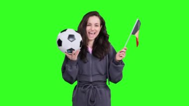 Gülümseyen genç bayan taraftar, elinde bir futbol topu tutarken Belçika bayrağıyla poz veriyor, yeşil izole edilmiş alanda takım zaferini kutluyor.