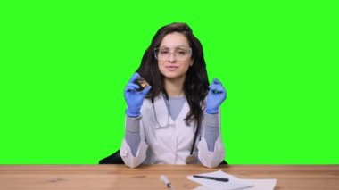 Steteskoplu, koruyucu eldivenli, üniformalı bir kadın doktor laboratuvarda elinde yeşil izole edilmiş bir arka planda aşı şişesi tutuyor. Sağlık Medikal Konsepti