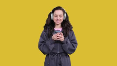 Cep telefonu ve daktilo ile müzik dinleyen mutlu genç kadın, sarı izole ekrana bakıyor.