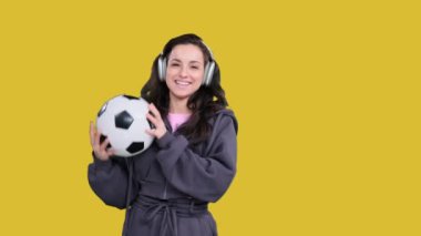 Gülen Kafkasyalı sporcu kadın futbol topunu tutarken kusuyor, sarı izole edilmiş kulaklıkla müzik dinliyor.