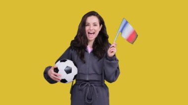 Futbol topu tutarken Fransız bayrağıyla poz veren genç ve mutlu bir bayan taraftar sarı izole edilmiş alanda takım zaferini kutluyor.
