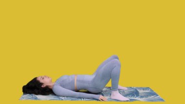 Sarı izole arka planda egzersiz minderinin üzerinde uzanırken ince ve sportif bir kadın spor yaparken. Vücut sağlığı kavramı