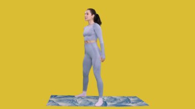 Spor giyim bölümünde idman yaparken çömelme egzersizi yapan pozitif bir kadın, sarı izole arka planda yerde duruyor. Fitness, spor, sağlıklı konsept