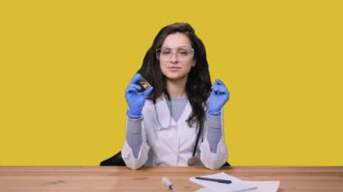 Steteskoplu, koruyucu eldivenli, üniformalı kadın doktor laboratuvarda elinde sarı izole edilmiş bir arka planda aşı şişesi tutuyor. Sağlık Medikal Konsepti