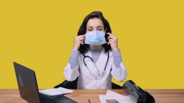 Sarı izole edilmiş arka planda dizüstü bilgisayarla çalışırken koruyucu yüz maskesi takan kadın doktor. Sağlık hizmeti, tıp konsepti