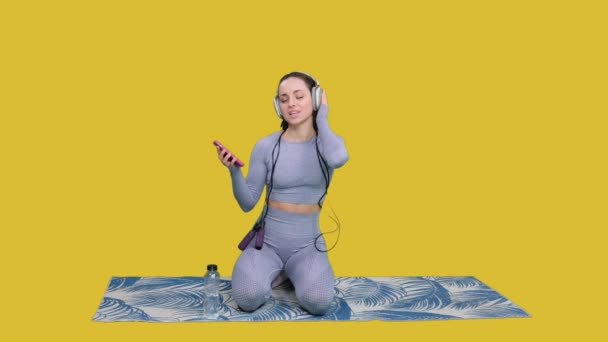 Gülümseyen Sportif Kadın Telefon Tutarken Kulaklıkla Müzik Dinliyor Sarı Izole — Stok video
