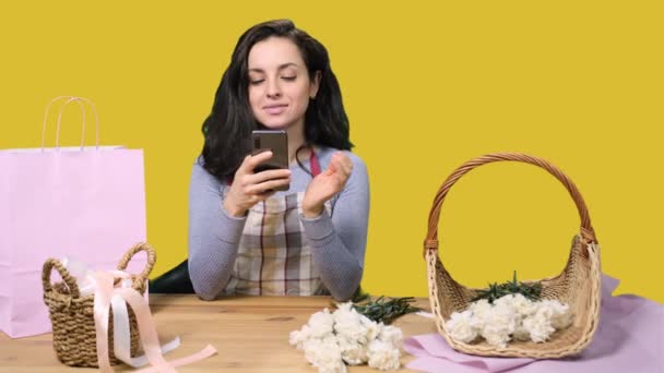 黄色い隔離された背景のワークショップでメッセージを読んでいる間 エプロンで幸せな女性の花屋 花配達 注文を作成する — ストック動画