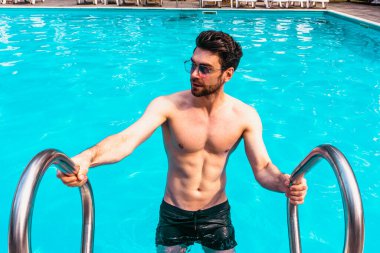 Güneş gözlüklü şık bir adam güneşli bir günde yüzmeye giderken dinleniyor. Uzayı kopyala Yaz zamanı, tatiller, yaşam tarzı konsepti